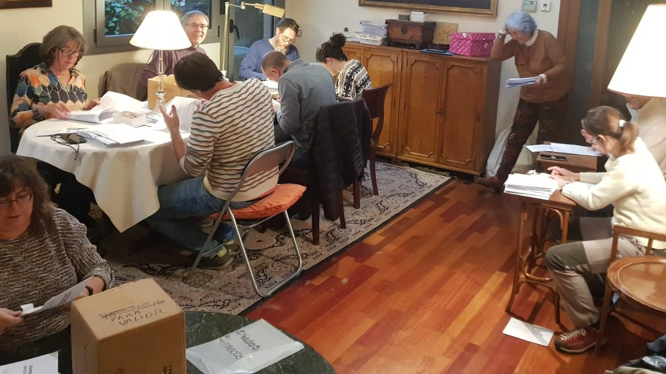 Un grupo de voluntarios revisa pliegos de firmas sentados alrededor de la mesa de un salón